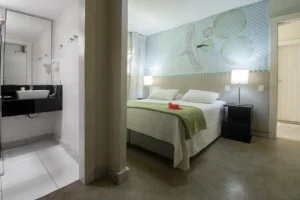 Suíte Standard vista do banheiro, com cama de casal e colcha verde