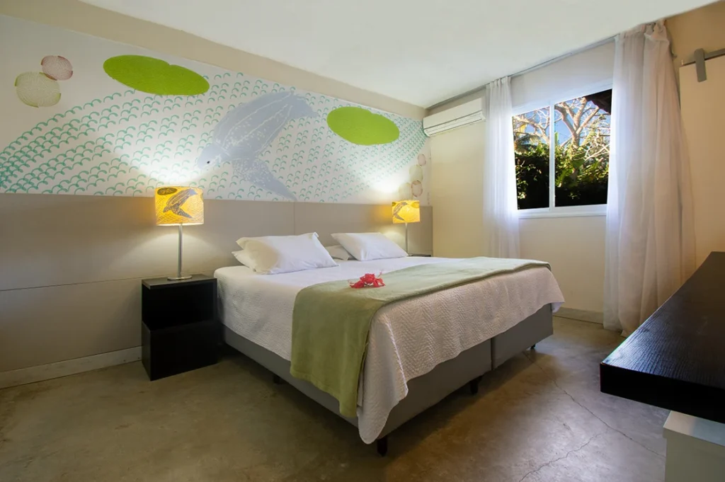 Cama queen da Suíte Superior Dupla, com abajures e janela para o verde