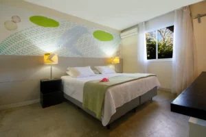 Cama queen da Suíte Superior Dupla, com abajures e janela para o verde