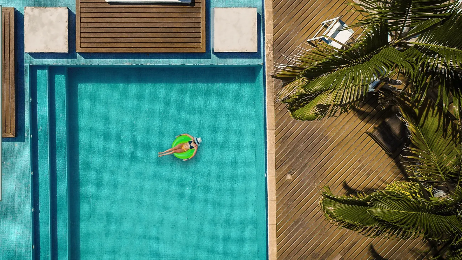 Piscina da nossa pousada no centro de Búzios, vista de cima, com deck de madeira e coqueiro